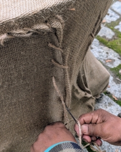 Then he sews the opening closed. There is a lot of tucking involved to make it neat, and a lot of stitching and knotting, but my crew has been covering these pieces with burlap every year for quite some time – they are all excellent burlap sewers.