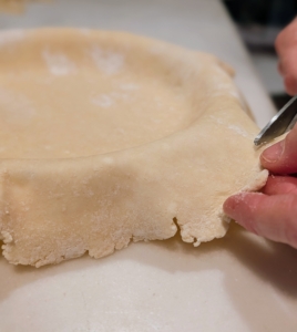 After pressing the dough into the plate, using kitchen shears trim the edge to one inch over and fold under, so it looks neat and tidy. Save the scraps for the decorations. Then put the plate into the fridge to chill.