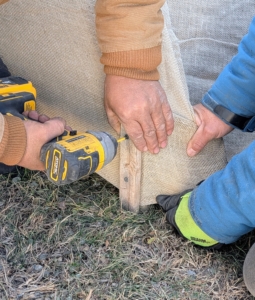 And Phurba screws the strips to the stakes, sandwiching the burlap in between.
