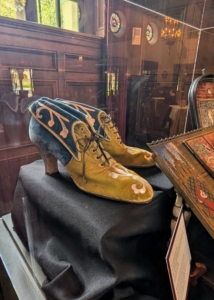 Also in the Music Room, a pair of Lucie's shoes. Shoes of this era had elongated silhouettes to emphasize narrow foot shapes. Decorative elements were also used and required snug fits to maintain structure.