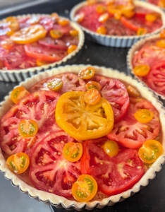 The tarts are garnished with cherry tomatoes and seasoned with salt and pepper before going in the oven.