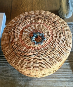 This basket was made by a Penobscot Nation basket weaver. It is made from black ash and sweetgrass. This basket is extra special because of the spiral weave pattern and the decorative star ring at the top.