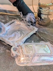 Here, Enma cleans two small trays. After rinsing off the silver cream, she washes the pieces with dish soap and water again to ensure all the cream is removed.