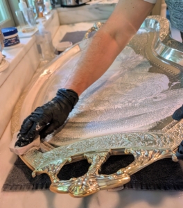 Enma does the same with this large serving tray. First she applies the cream. The silver will start to brighten as it is rubbed. Always use silver polishes that are non-abrasive, and opt for formulas, such as creams and gels instead of sprays.