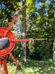 A hay tedder spreads and fluffs the hay in a uniform swath. It uses a rotary motion to grab the hay with spinning tines that cast it out the back of the machine.