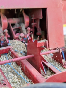 The motor helps to move and propel the bales into the wagon. A measuring device – the spiked wheel – is turned by the emerging bales. It measures the amount of material that is being compressed and then the knotters wrap the twine around the bale and tie it off.