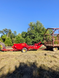 A baler is a piece of farm machinery that compresses the cut and raked crop into compact bales that are easy to handle, transport, and store. The baler is attached to the tractor, and then the hay wagon is attached to the baler.