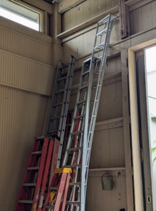 Ladders of various sizes rest against one wall close to one set of large barn doors.