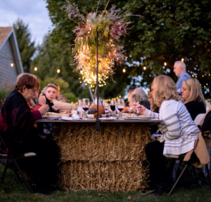 This photo is of a humble backyard dinner for 20 guests celebrating harvest. Custom stained plywood sat atop straw bales from Brian's farm created a generous table to host the dinner. An over the table rod and stargazer lights with foraged foliage from the garden helped usher in the whimsy.