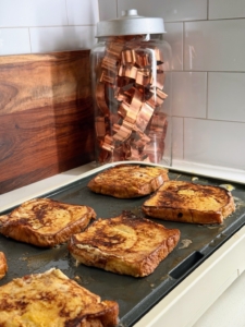 Brian makes French toast on my new Kitchen Electrics 22-inch by 12-inch griddle next to an apothecary jar from Martha by Mail filled with more copper cookie cutters.