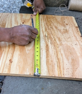 The crew cuts spare plywood into custom lids to fit over various pieces. Pete measures the diameter of pot's top and then marks it on the plywood before cutting.
