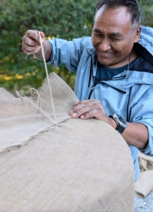 After the side edge, Pete sews the top closed, tucking the excess burlap in and pulling taut as he goes.